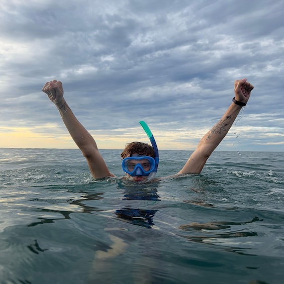 A person swimming in the ocean with arms raised, wearing a snorkel mask and goggles. 2