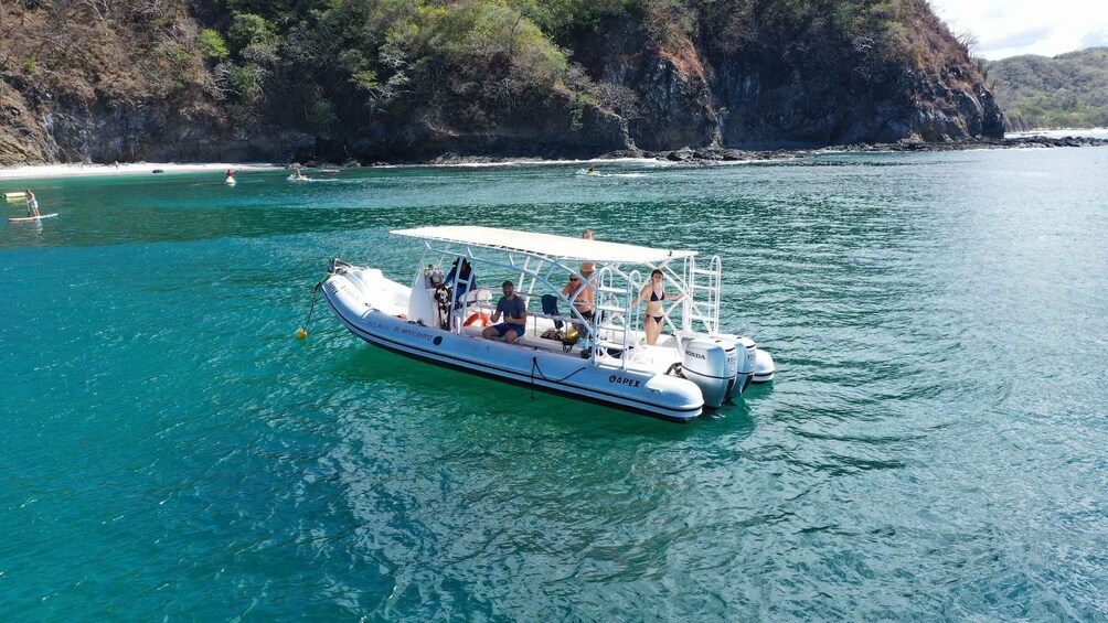 A boat on turquoise water with a rocky coastline in the background. 2