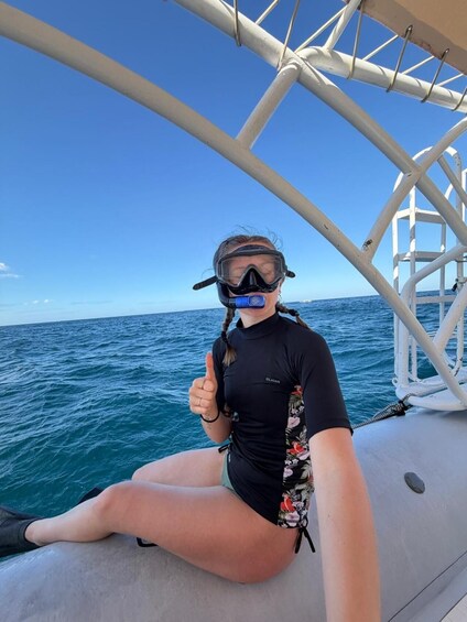 A person sitting on a boat, wearing a wetsuit and snorkel mask, with the ocean and sky in the background. 3