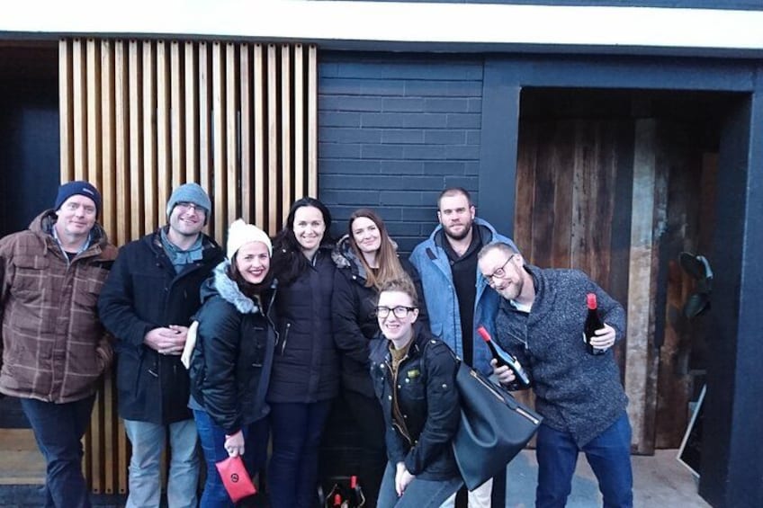 A group of people standing in front of a building with a wooden slat wall and a dark door. 2