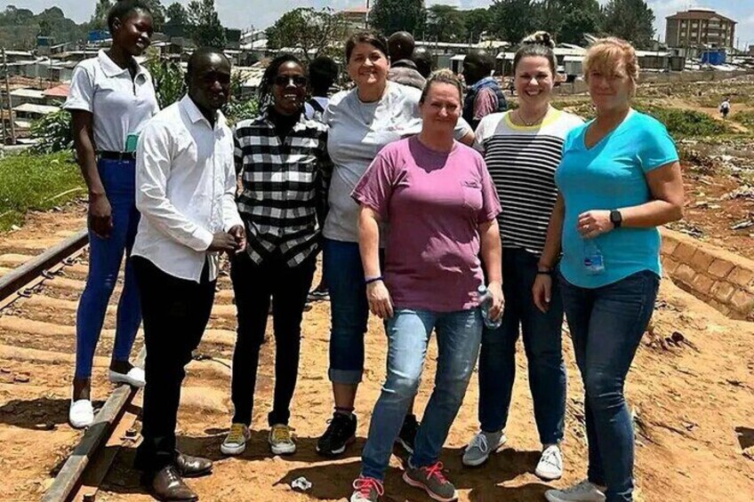Un groupe de personnes se tient sur un chemin de terre, avec des voies ferrées en arrière-plan. 5