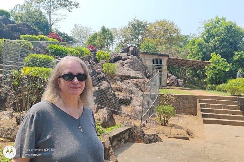 A person standing in front of a rocky landscape with a metal fence and a building with a roof. 4