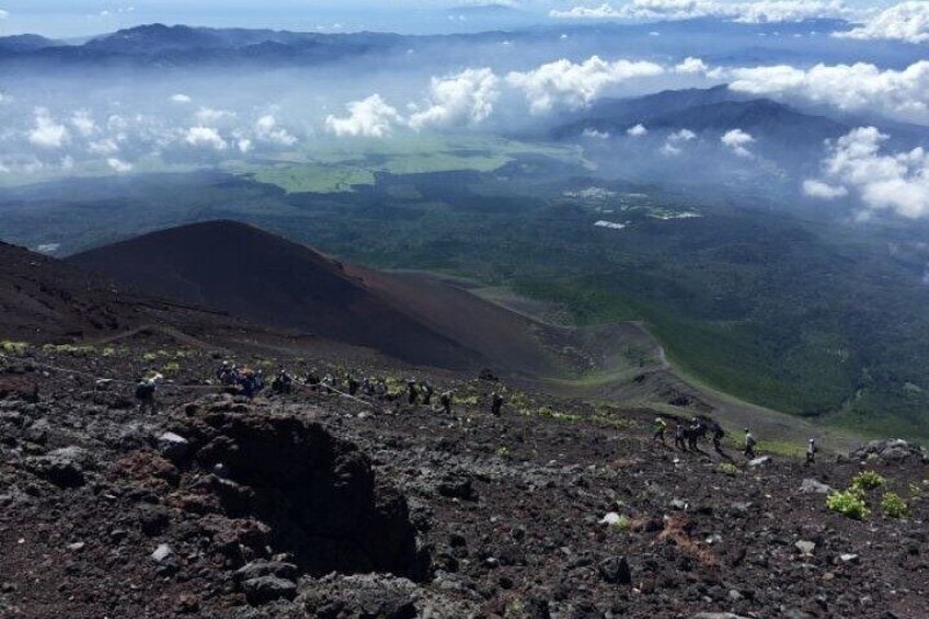 A volcanic landscape with hikers, a crater, and a valley with clouds above. 3