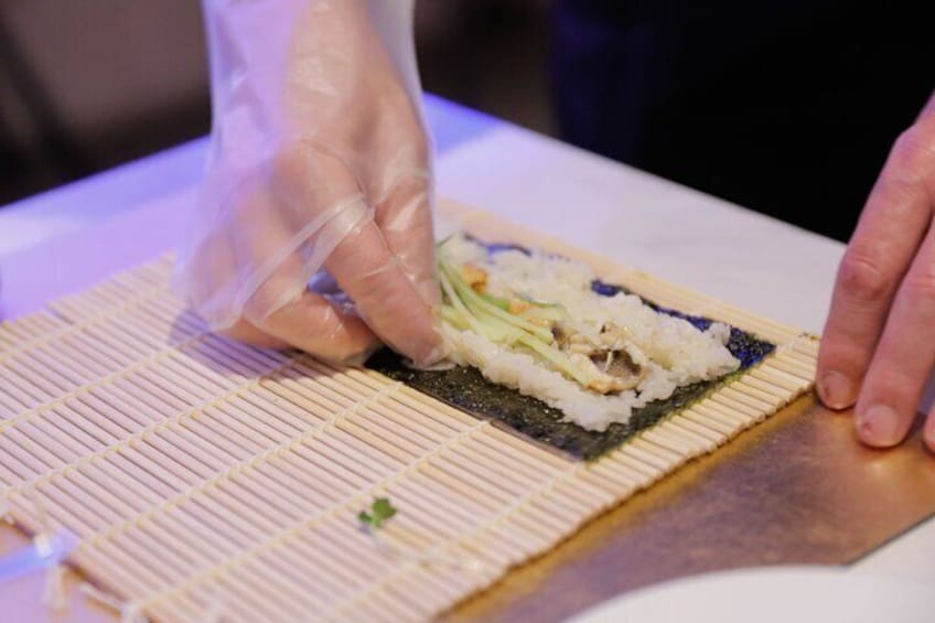 A person preparing sushi with rice and vegetables on a bamboo mat. 1
