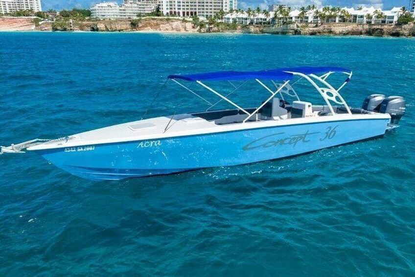 Een blauwe speedboot genaamd 'Concept 36' op een kalme zee, met een strand en gebouwen op de achtergrond. 1