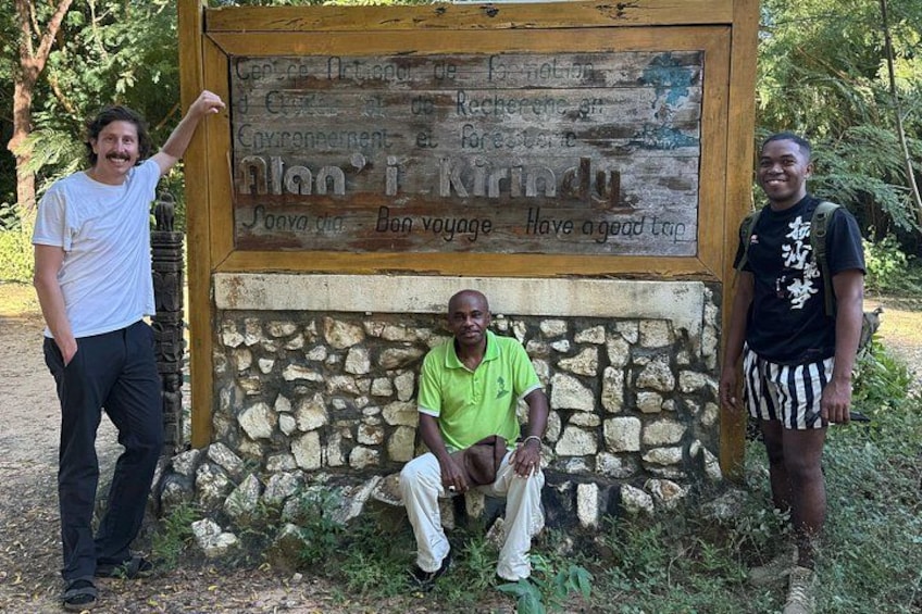 A wooden sign with text, three people, and a stone wall. 4