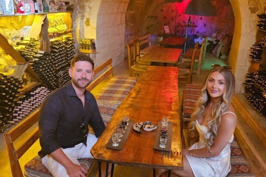 A wine cellar with wooden racks of wine bottles, a long wooden table, and a cozy seating area. 2