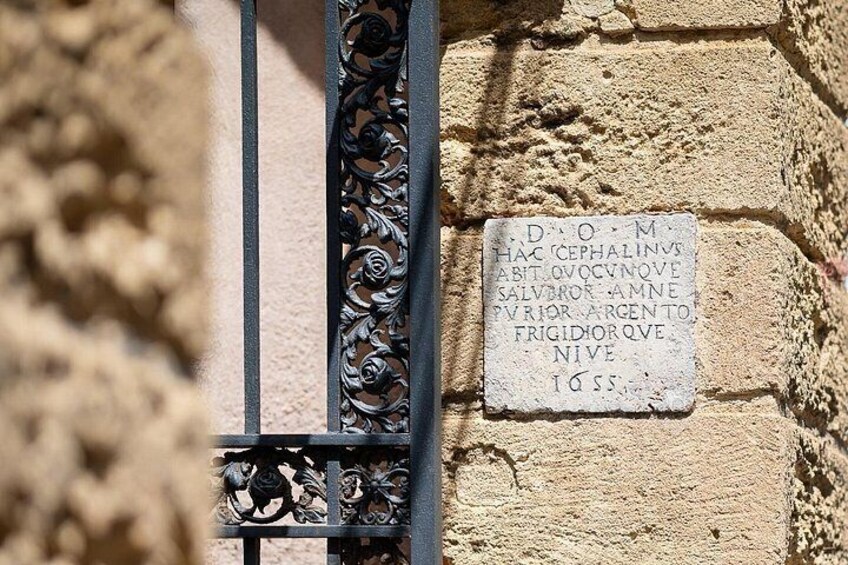 A stone wall with a metal gate and a plaque with inscriptions. 3