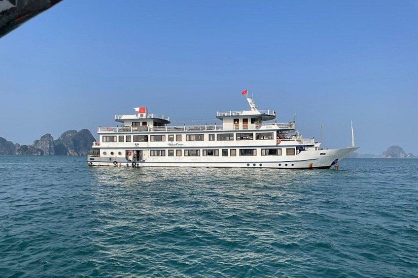 A large white river cruise ship with multiple decks and a flag on top, sailing on a body of water with rocky landforms in the background. 1