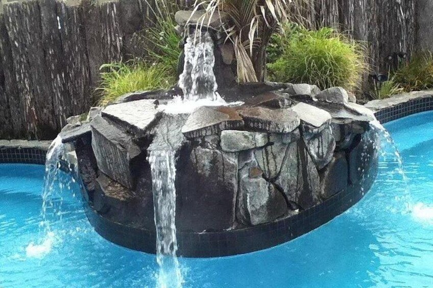 A circular rock formation with a waterfall in a swimming pool. 1