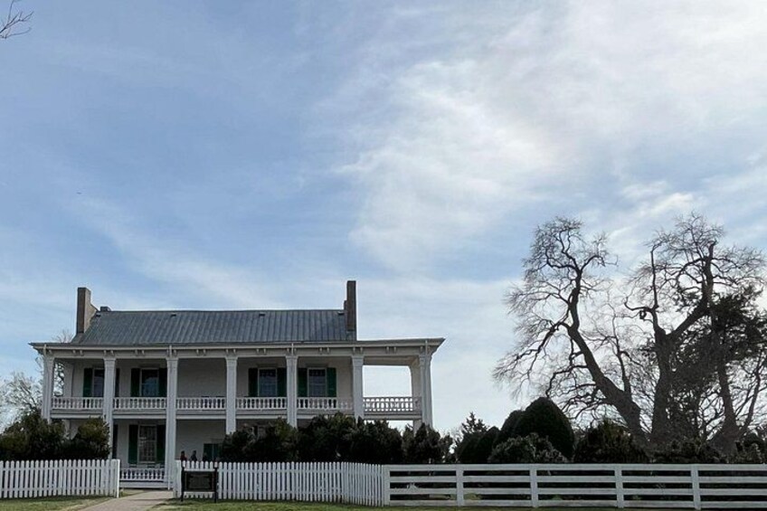 A large white house with a porch, surrounded by a white picket fence, under a partly cloudy sky. 2