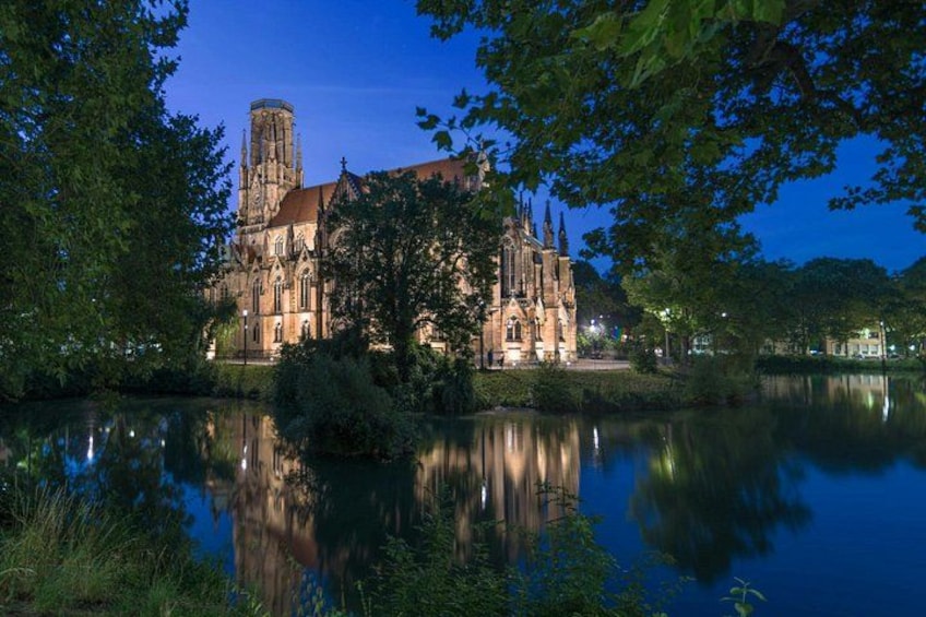 Una cattedrale gotica con un'alta torre, circondata da alberi e specchiata in acque calme. 2