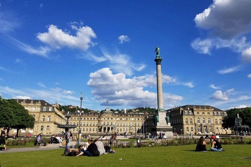 Un'ampia piazza aperta con un monumento imponente, circondata da edifici storici e persone sedute sull'erba. 3
