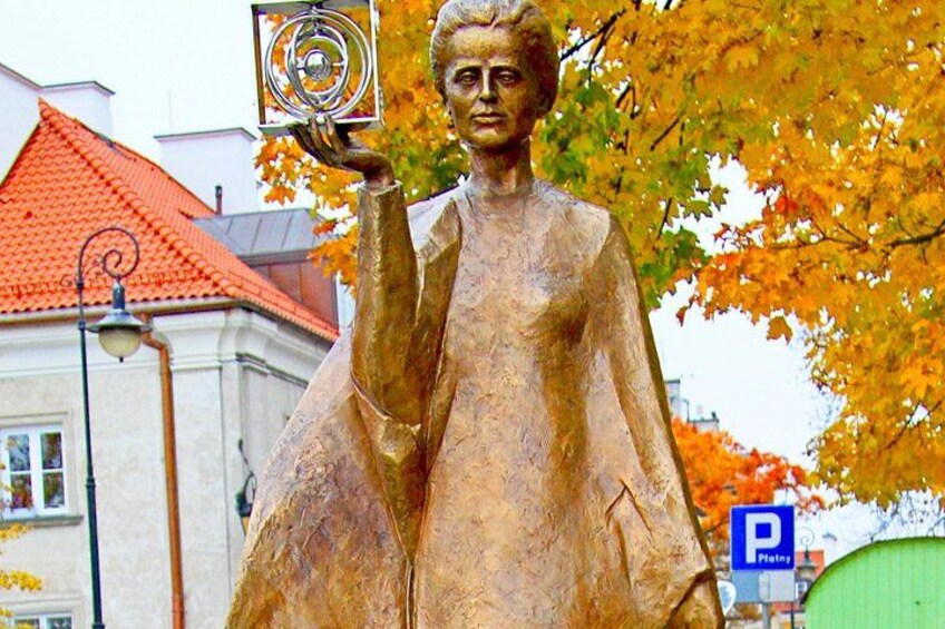 A bronze statue of a woman holding a book, with autumn leaves and a building in the background. 4