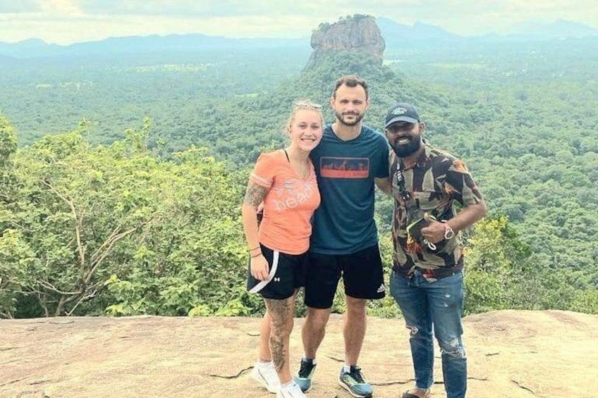 Three people standing on a rocky outcrop with a forested valley in the background. 4