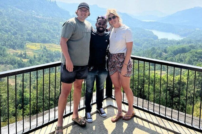 Tres personas de pie en un balcón con una vista panorámica de montañas y un lago. 2