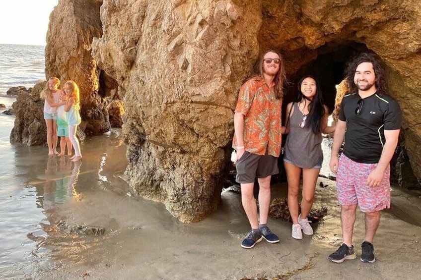 Eine Gruppe von Menschen steht vor dem Felseneingang einer Höhle am Strand. 2