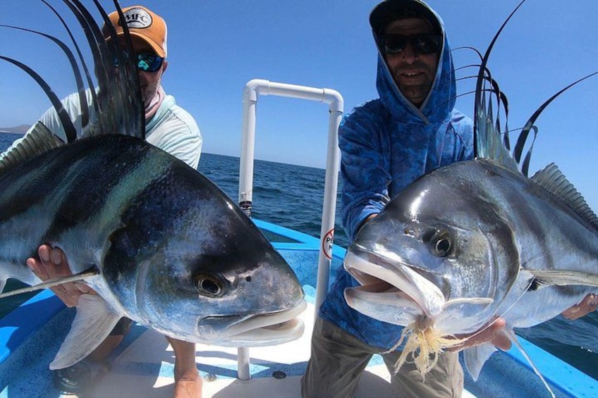 Two people holding large fish on a boat. 1