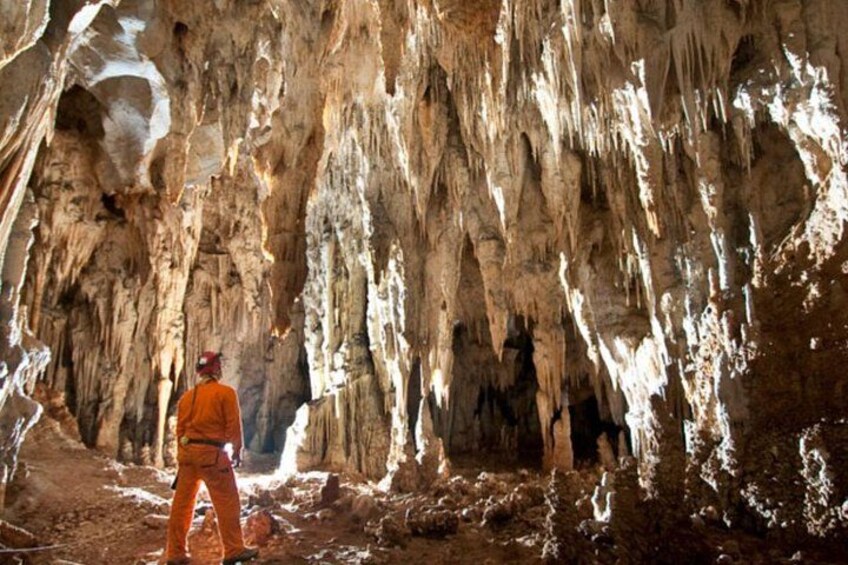 A person in orange clothing standing in a cave with stalactites. 3