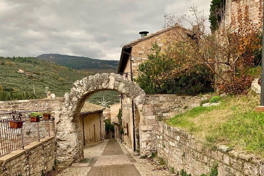 A stone archway leading to a pathway, surrounded by stone walls and vegetation. 2