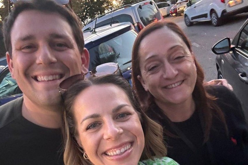Three people in a parking lot with cars and trees in the background. 1