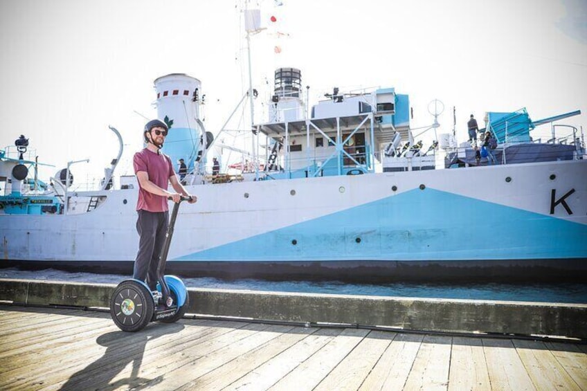 A person riding a Segway on a wooden dock with a large ship in the background. 5