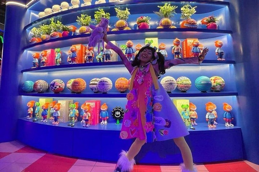 Una persona con un vestido colorido posa frente a una vitrina con diferentes figuritas y objetos decorativos. 2
