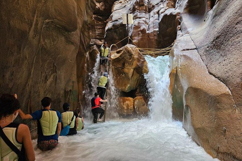 A group of people climbing a rocky waterfall in a canyon. 1