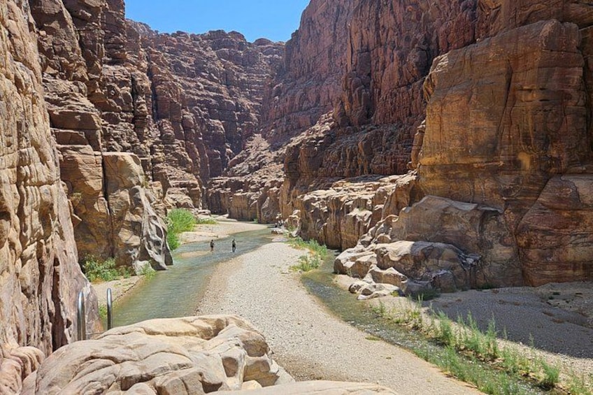 A canyon with a narrow river, rocky cliffs, and a few people walking. 5