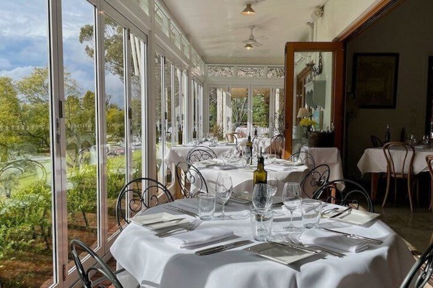 A restaurant with tables set for dining, large windows, and a view of greenery. 5