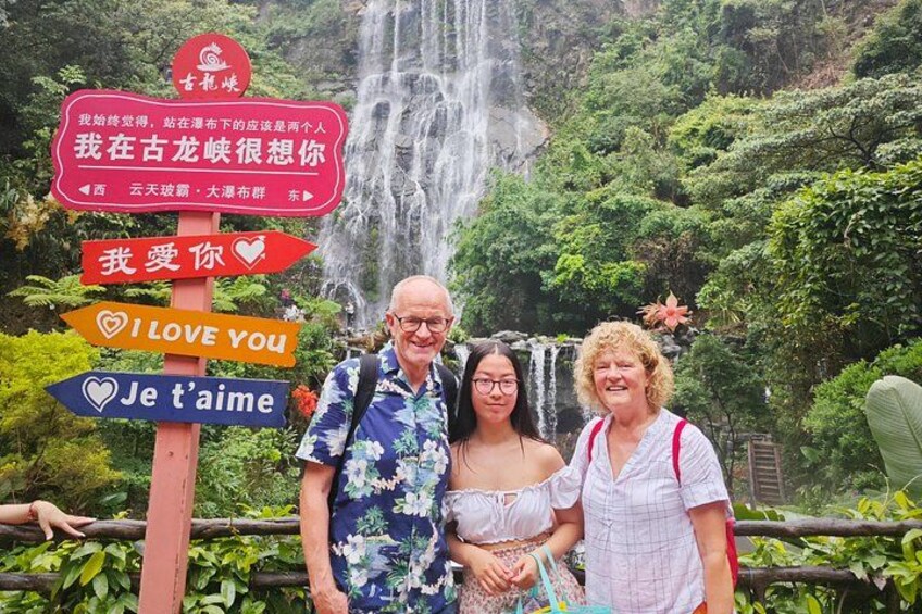Una cascada, un cartel con varios idiomas, y tres personas de pie frente a ella. 5