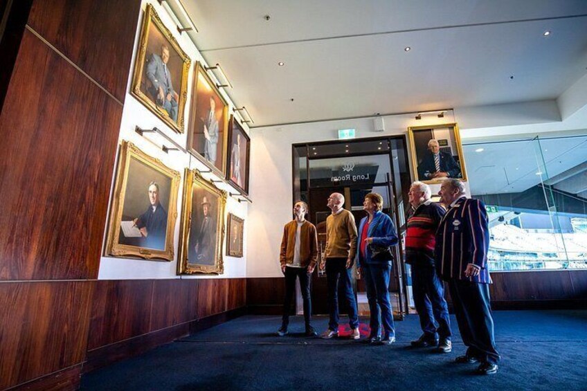 A group of people standing in a hallway with framed portraits on the wall. 2