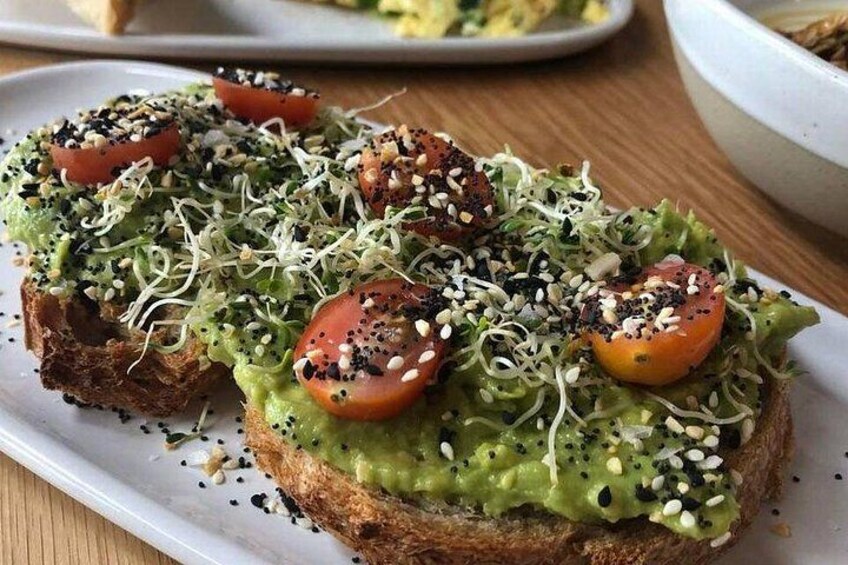 A plate with a sandwich topped with avocado, tomato slices, sprouts, and seeds. 2