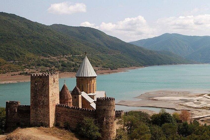 Un castillo histórico con una torre, rodeado por un lago y montañas. 3