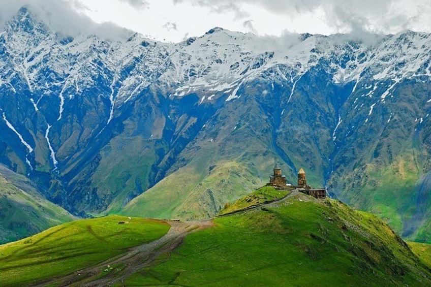 Un paisaje montañoso con un valle verde, un camino de tierra y una pequeña construcción de piedra. 1