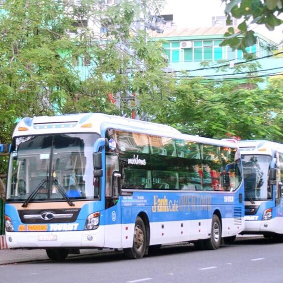 Two buses on a road with trees and buildings in the background. 3