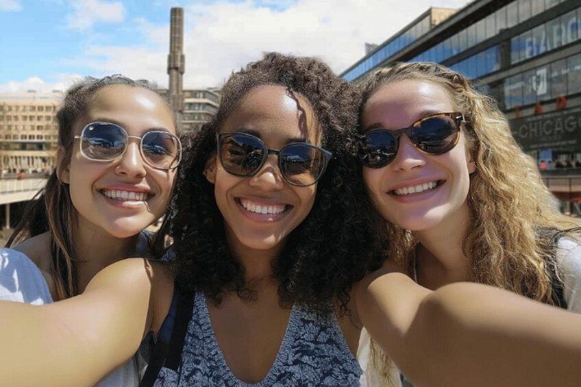 Tres personas tomándose un selfie en un entorno urbano, con edificios y cielo despejado al fondo. 5