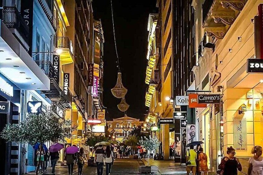 A nighttime street scene with illuminated buildings, hanging lanterns, and pedestrians. 2