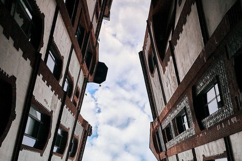 A narrow street between two buildings with traditional architecture, featuring arched windows and decorative brickwork. 2
