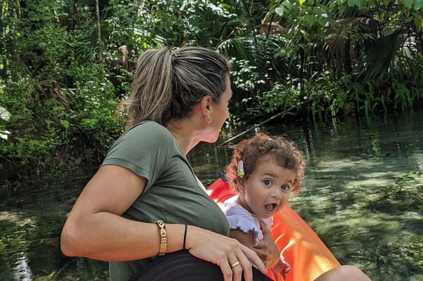Een vrouw in een groene blouse houdt een kind vast in een boot op een rivier, omringd door weelderige begroeiing. 4