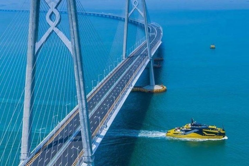 Un gran puente colgante con cables y una carretera, un barco amarillo en el agua y una pequeña boya. 1