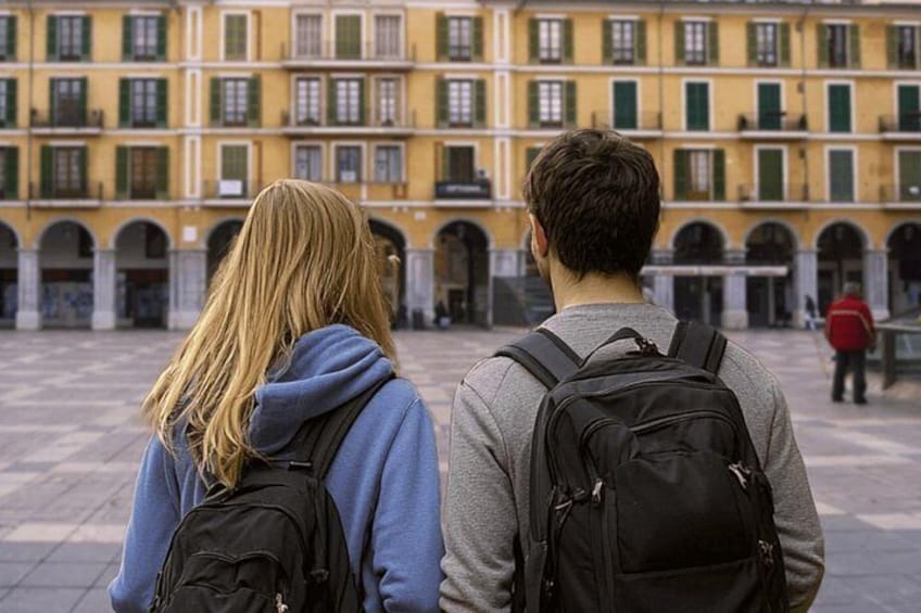 Two people with backpacks in a courtyard with yellow buildings. 2