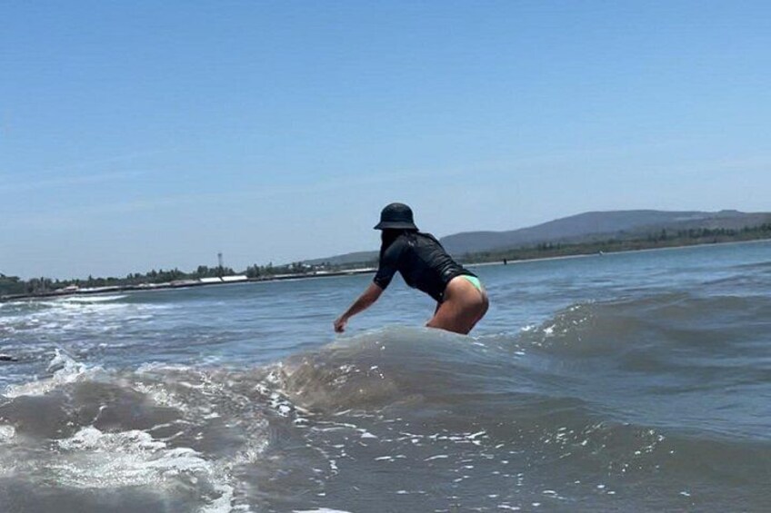 A person surfing on a wave in a body of water with a clear sky and distant mountains. 4
