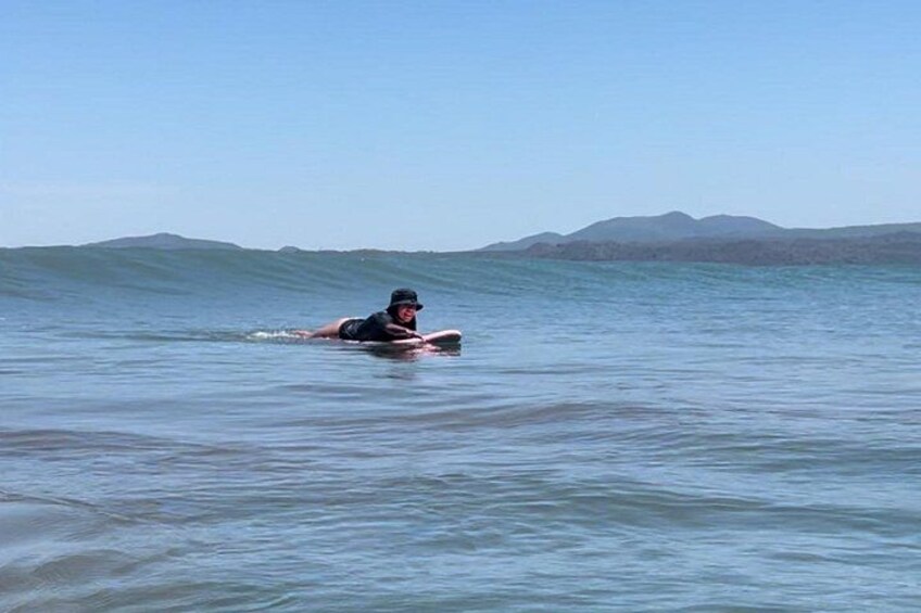A person lying on a surfboard in calm ocean waters with distant mountains. 3