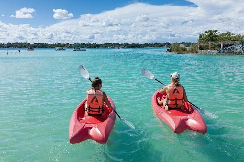 Twee personen kajakken op turquoise water, met een heldere lucht en land in de verte. 3