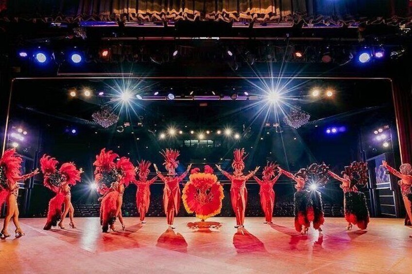 A stage with performers in red costumes, a large flower prop, and bright stage lighting. 4
