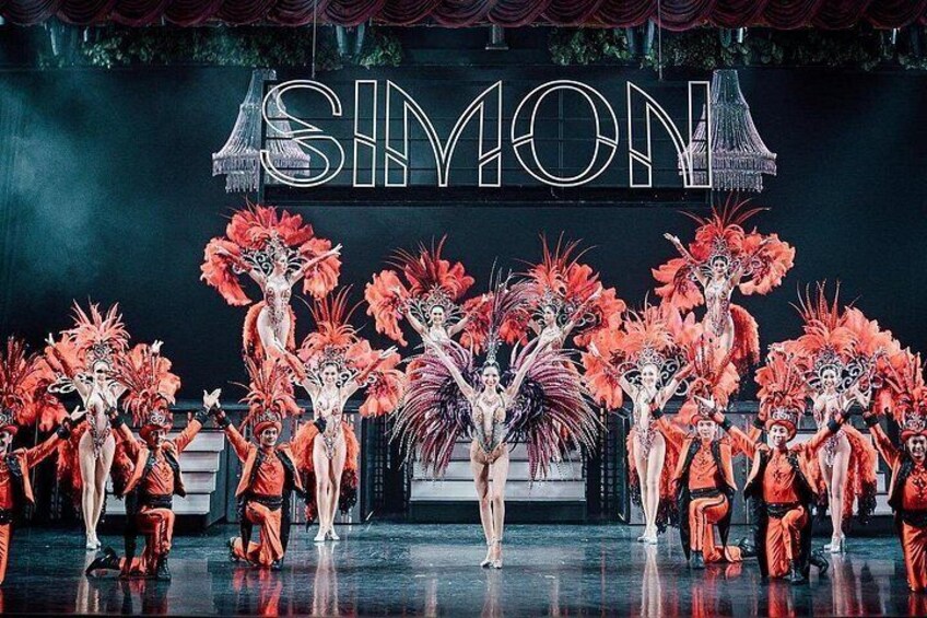 A stage with performers in elaborate costumes and a backdrop with the word 'SIMON' prominently displayed. 2