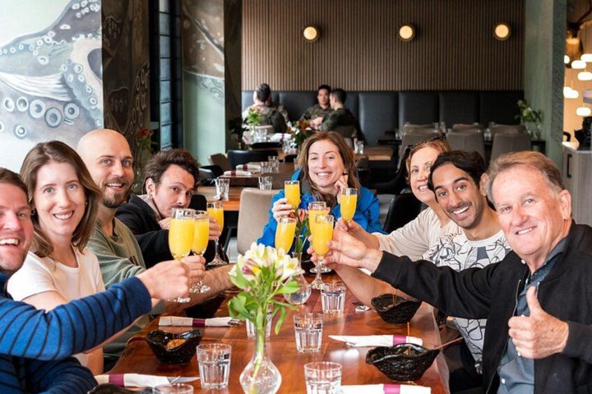 A group of people toasting with drinks at a restaurant table with a vase of flowers. 1