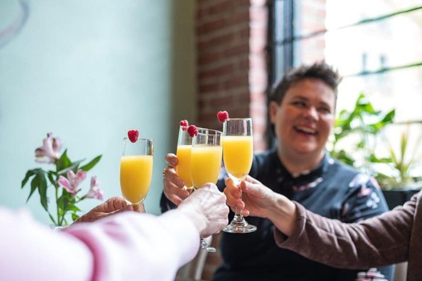 Three people toasting with glasses of orange juice garnished with raspberries. 2