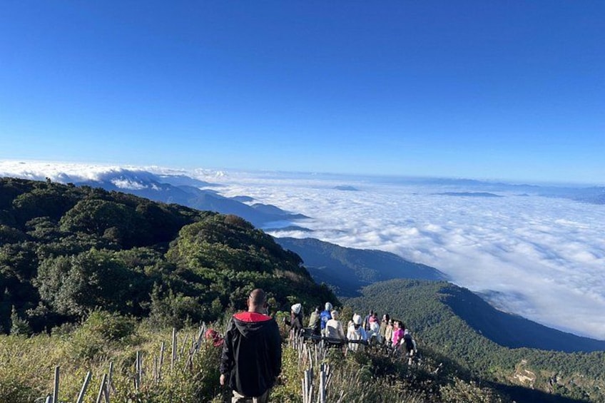 Een groep mensen op een bergpad met uitzicht op de wolken daaronder. 4